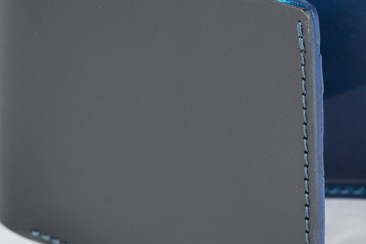 Detail kontrastního tyrkysového sedlářského švu po hraně peněženky Winston