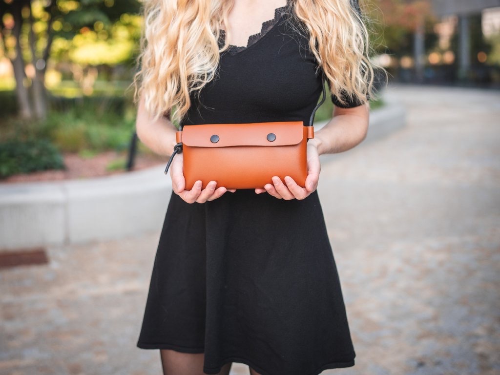 Žena nosí koženou kabelku Laura v koňakové crossbody na dlouhém černém popruhu