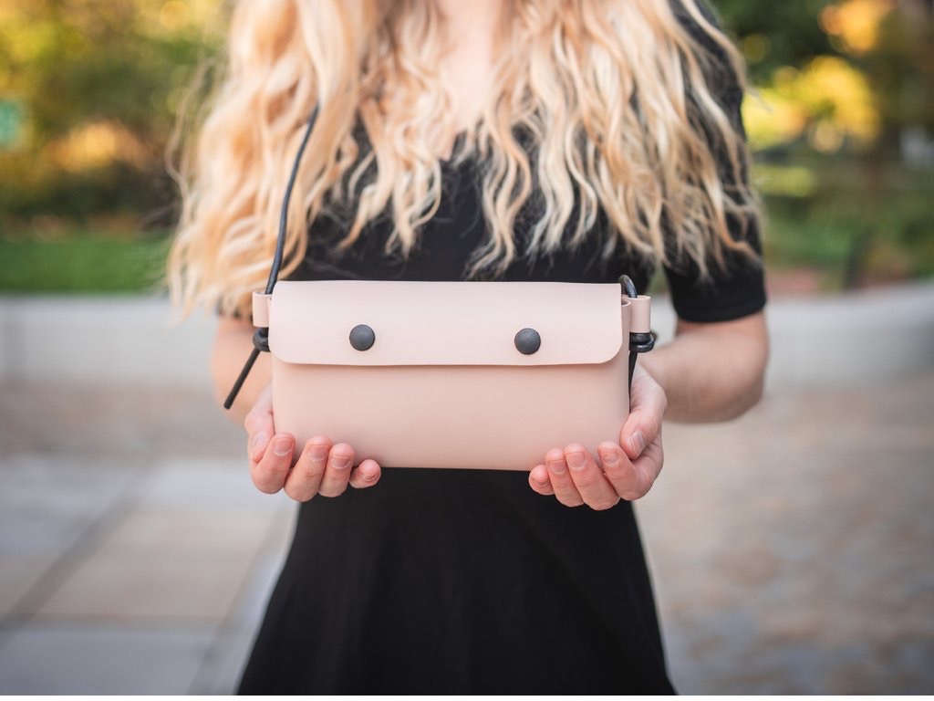 Žena nosí koženou kabelku Laura v pudrové crossbody na dlouhém černém popruhu