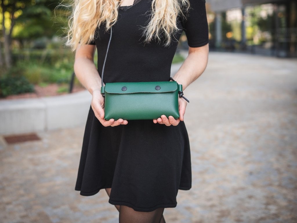 Žena nosí koženou kabelku Laura v zelené crossbody na dlouhém černém popruhu