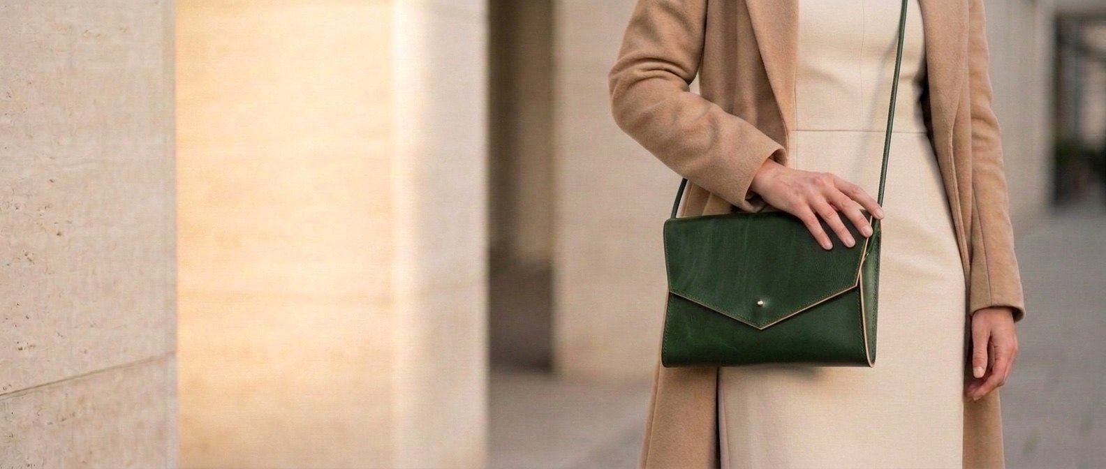 Žena v krémových šatech a kabátě nese zelenou koženou kabelku Mia 2.0 crossbody na tenkém popruhu