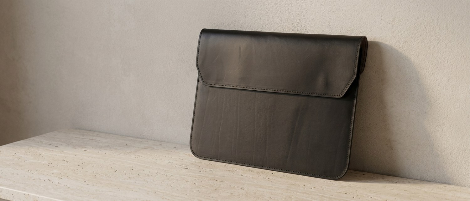 Černé kožené pouzdro na notebook 14″ z usně Buttero na tmavém ořechovém stole, vedle hrana notebooku