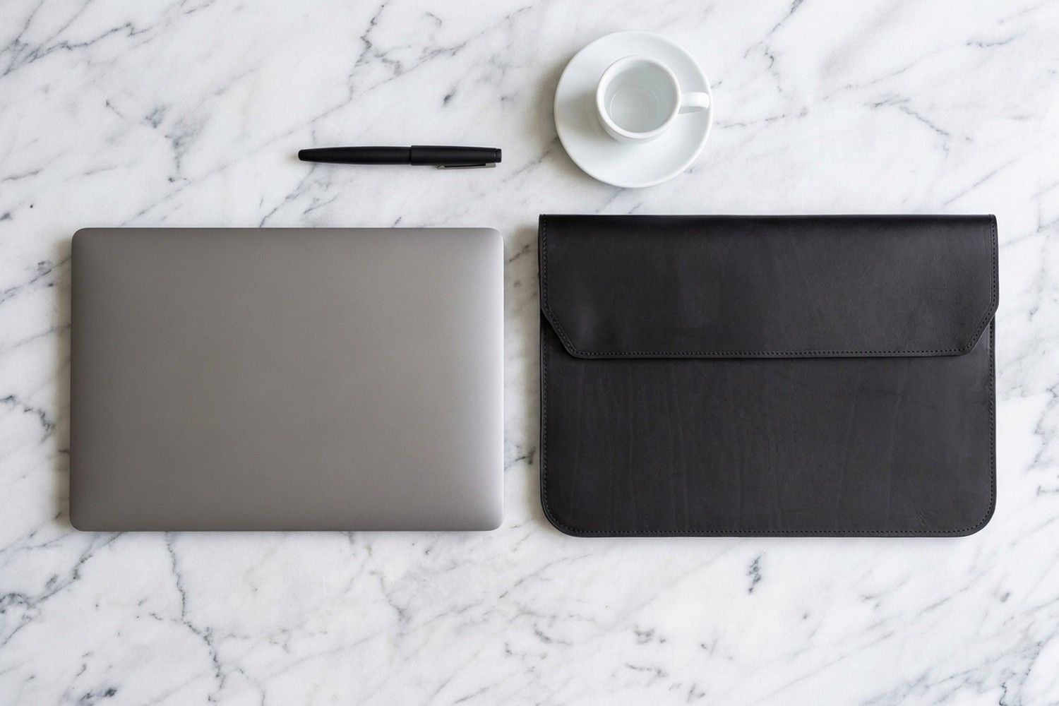 Černé pouzdro vedle notebooku 14″ na mramorovém stole, plnicí pero a espresso
