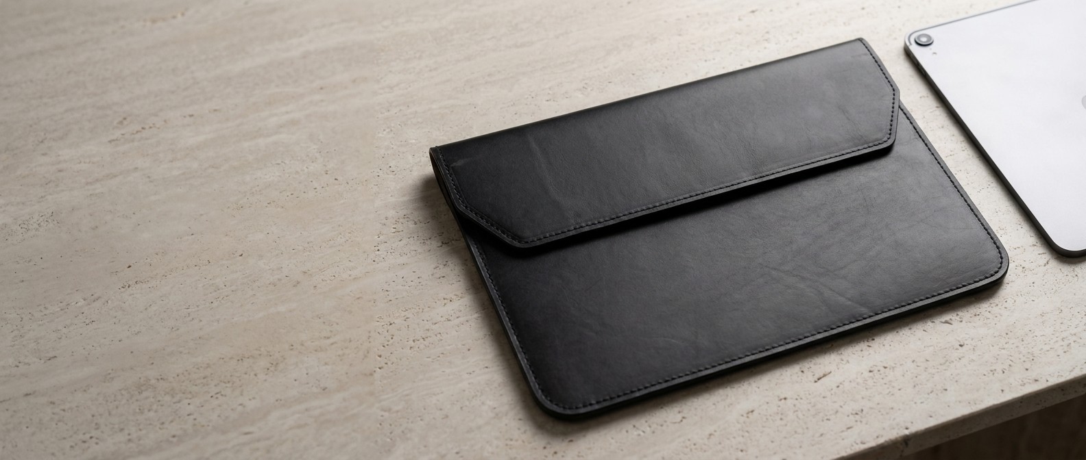 Černé kožené pouzdro na tablet 11″ z usně Buttero na travertinovém stole, vedle hrana tabletu
