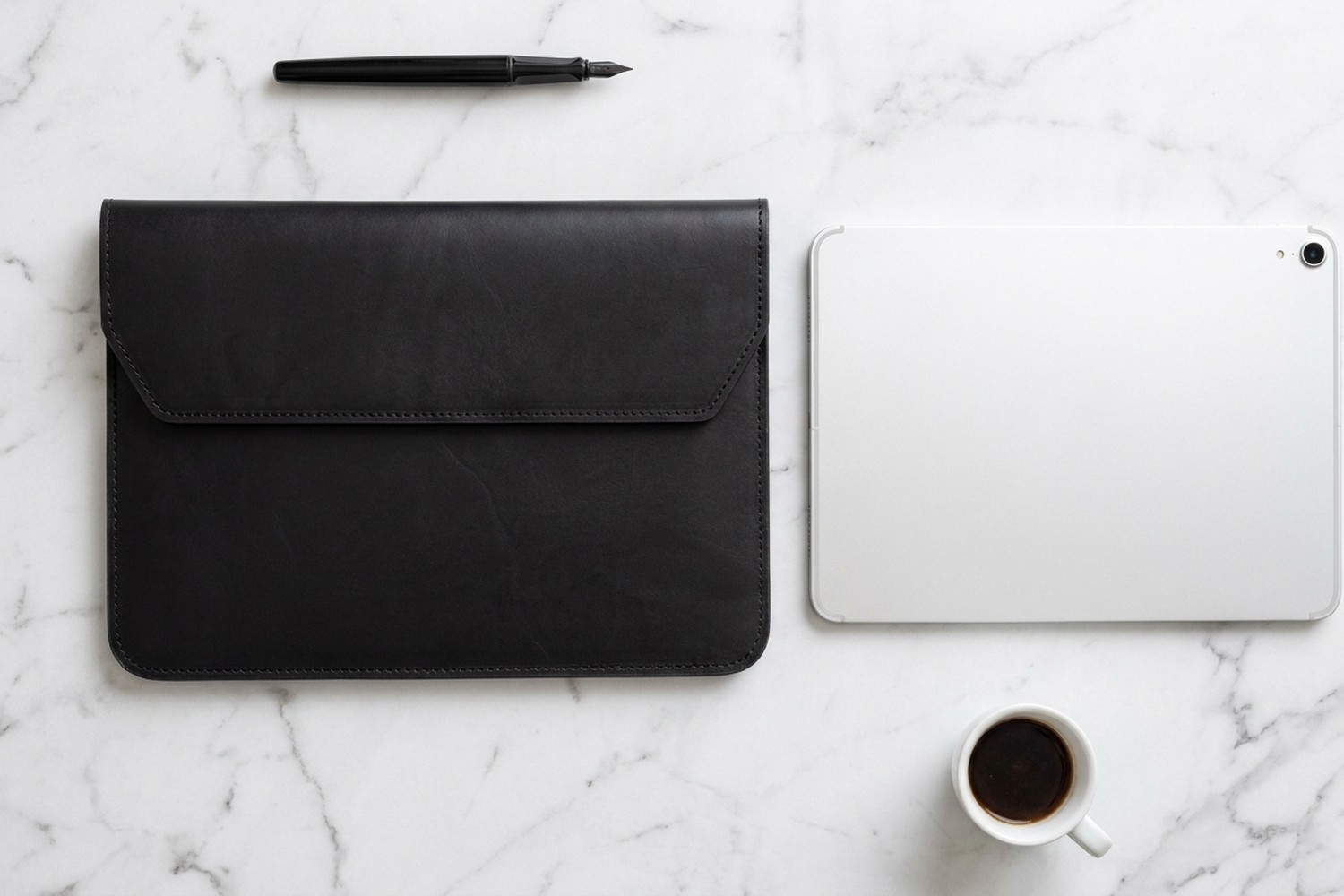Černé pouzdro vedle tabletu 11″ na mramorovém stole, plnicí pero a espresso