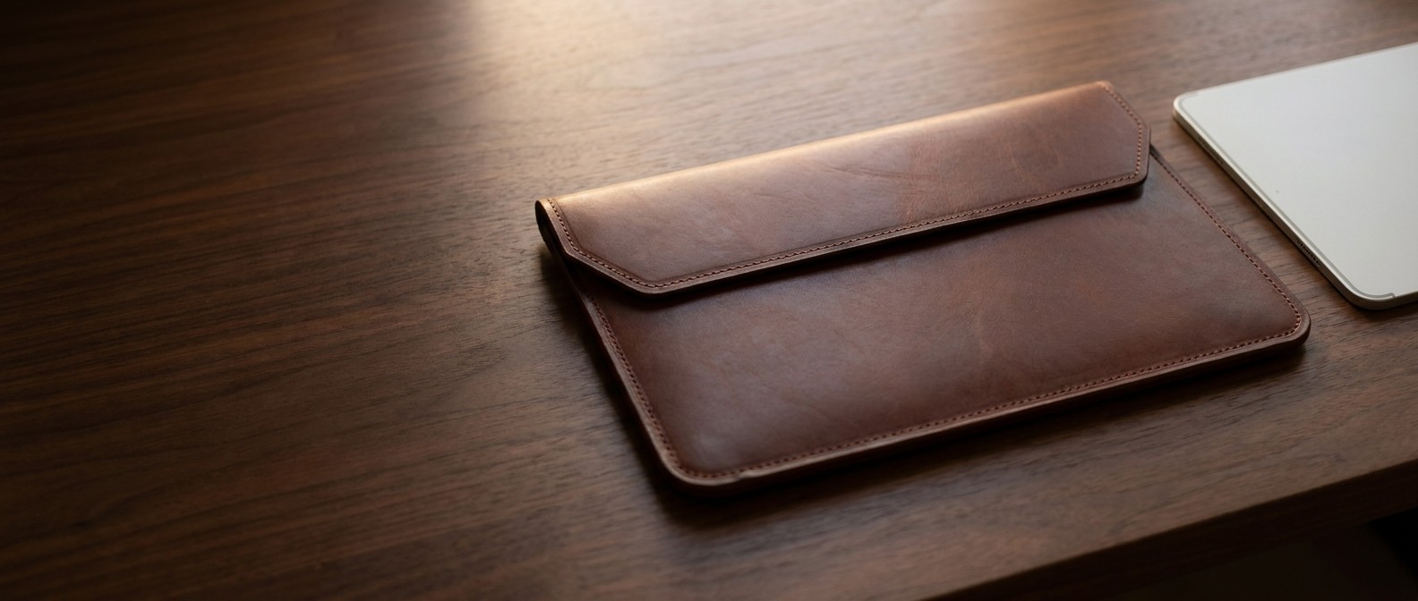 Hnědé kožené pouzdro na tablet 11″ z usně Buttero na ořechovém stole, vedle hrana tabletu