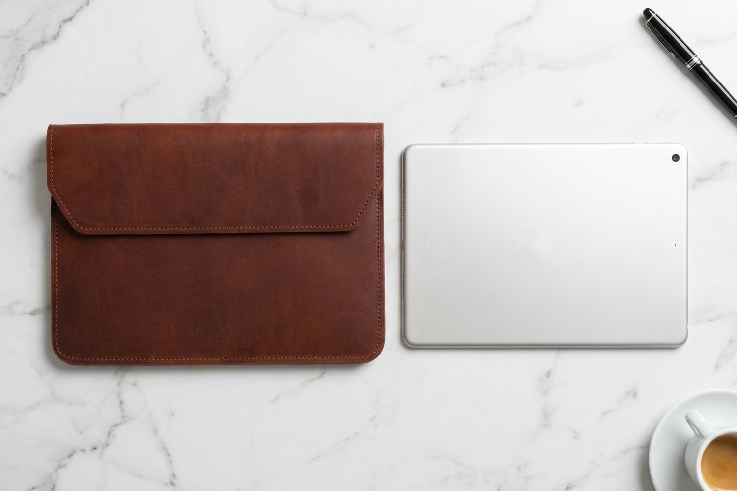 Hnědé pouzdro vedle tabletu 11″ na mramorovém stole, plnicí pero a espresso