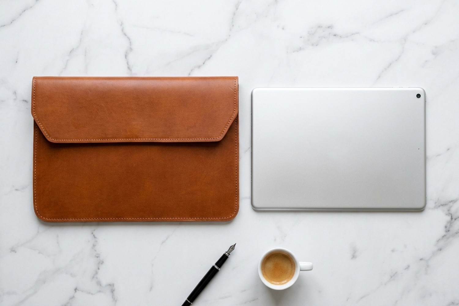 Koňakové pouzdro vedle tabletu 11″ na mramorovém stole, plnicí pero a espresso