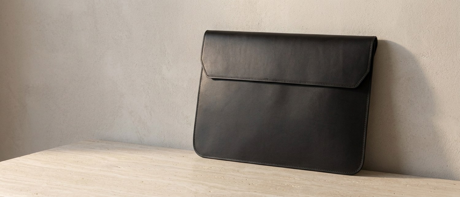 Černé kožené pouzdro na notebook 15″ z usně Buttero na tmavém ořechovém stole, vedle hrana notebooku