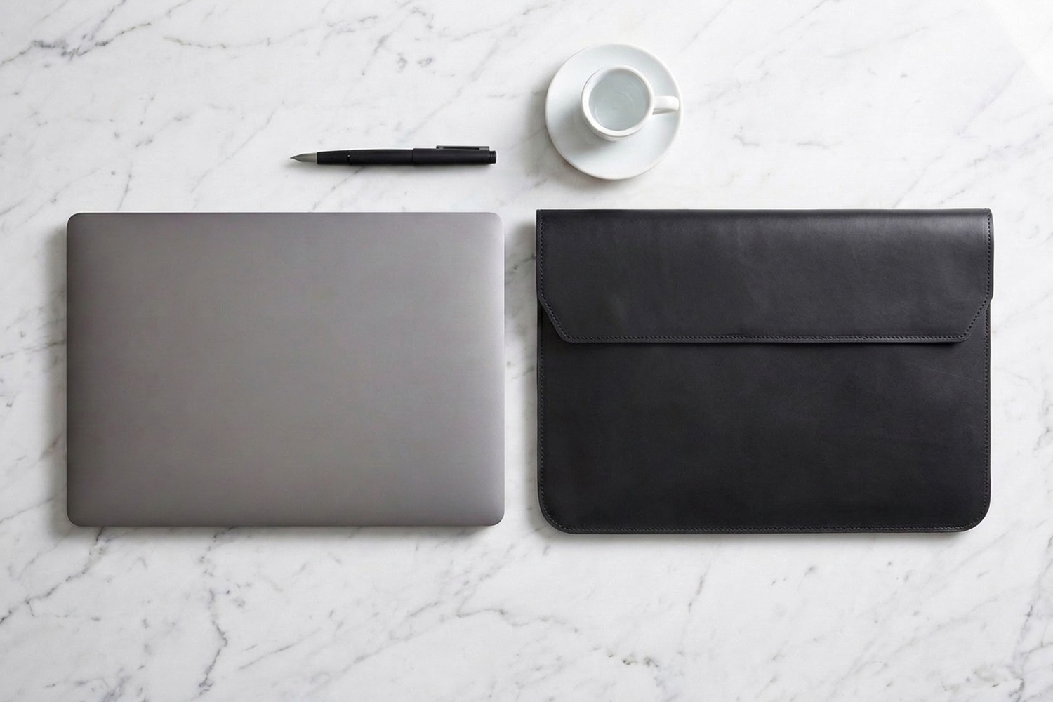 Černé pouzdro vedle notebooku 15″ na mramorovém stole, plnicí pero a espresso