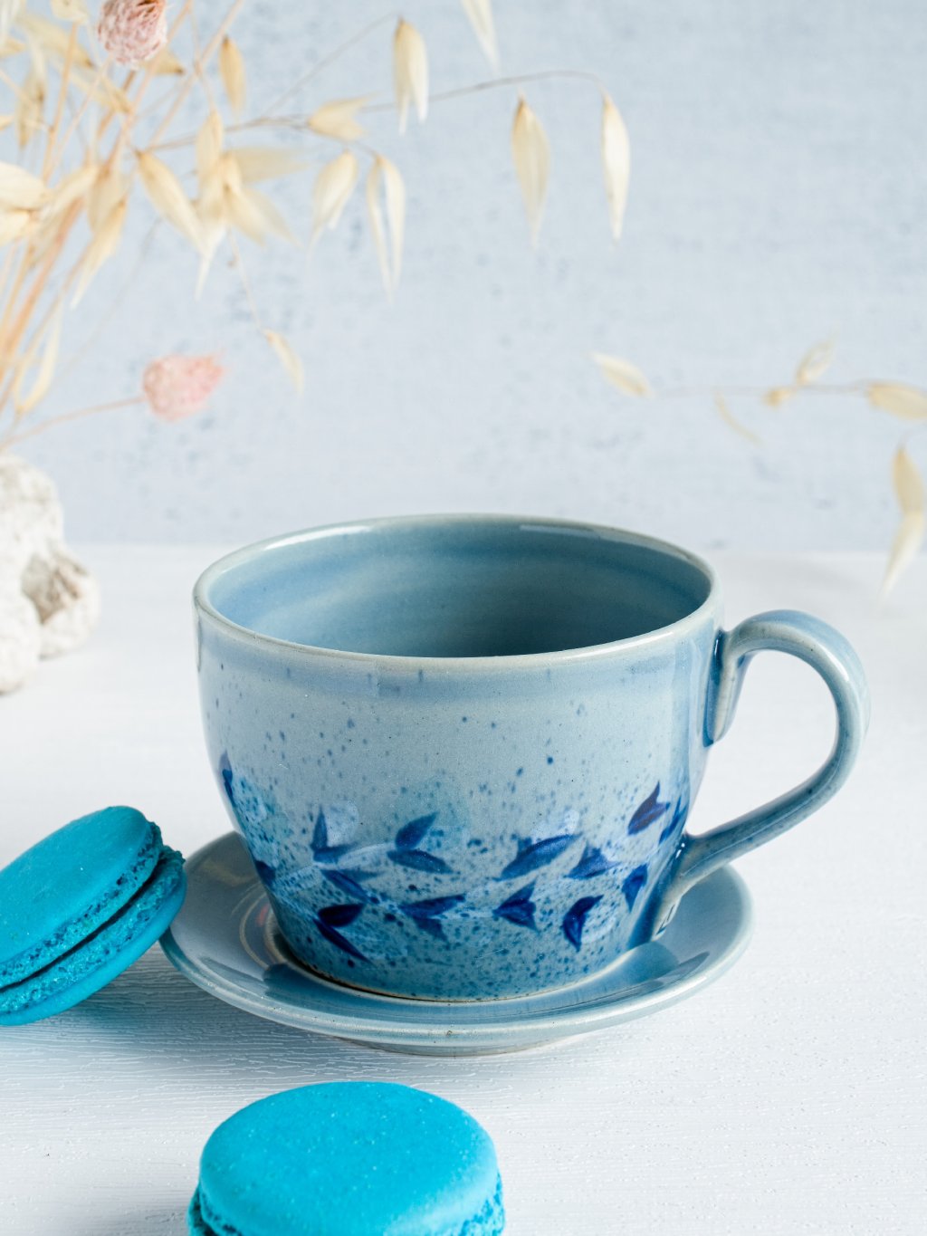 Modrý keramický šálek s podšálkem Poletující lístky – tmavě modrý listový dekor, lesklá glazura.