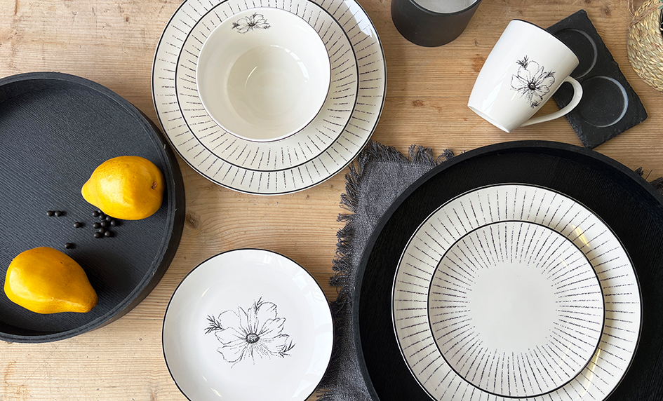 Moderní porcelánová sada Linea Dash s černým dekorem čárek a motivem květu na dřevěném stole.