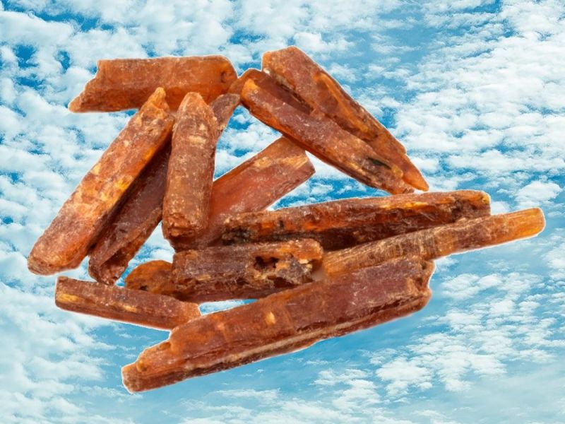 Oranžový kyanit -krystaly v pozadí modré nebe s bílými mráčky.