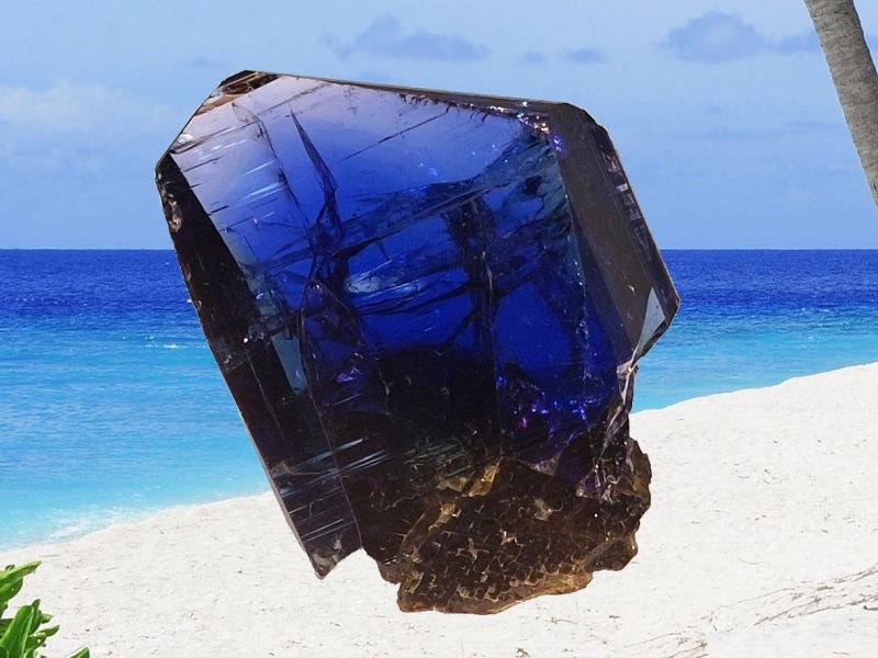 Tmavě modrý krystal tanzanitu, na pozadí pláž a moře.