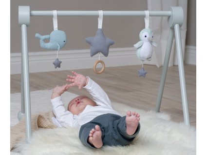 Dieťa ležiace na podložke pod drevenou hrazdou s plyšovými hračkami