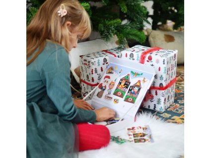 Dieťa sa hrá s magnetickou knihou s vianočnými motívmi pri stromčeku.