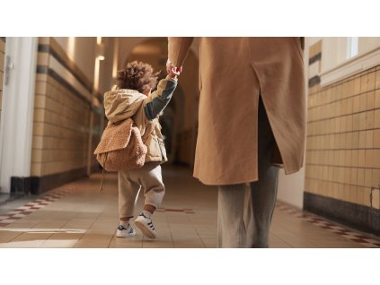 Dieťa kráčajúce s rodičom po chodbe, na chrbte má hnedý teddy ruksáčik Jollein