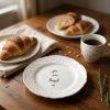 Warm, inviting kitchen scene bathed in soft, natural light A polka dot plate with elegant lettering rests on a rustic wooden table amidst a casual brunch spread Beside it, a half eaten croissant and a steamin