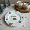 Close up lifestyle shot featuring a whimsical, winter themed dining table, where a white ceramic plate with a cartoon pig is set among playful festive decorations; A soft, diffused light creates a warm, invit
