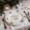 Close up of a festive holiday table setting with a whimsical, hand painted plate featuring a flying pig design as the focal point; the table is adorned with a crisp white linen tablecloth, complemented by sil