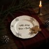 A cozy Christmas Eve dinner setting, featuring a white snowflake patterned plate with the inscription Takhle chutnají Vánoce u Bianky as the centerpiece Soft, warm candlelight flickers across a rustic wooden