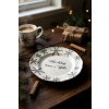 Close up lifestyle shot of a pristine white plate, adorned with delicate black snowflakes and Czech script, nestled amidst a cozy Christmas scene Warm, diffused sunlight streams through a nearby window, casti