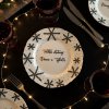 A beautifully decorated holiday dining table set for Christmas Eve dinner, a white plate with black snowflake designs and text Tekhle chutnají Vánoce u Tejkalu centered in the frame, surrounded by sparkling s