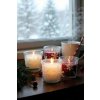Soft, diffused daylight streams through a snow dusted window, illuminating a cozy kitchen scene A rustic wooden countertop holds a small cluster of glass jar candles adorned with delicate, hand painted white