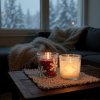 A cozy winter evening scene, focus on a rustic wooden coffee table adorned with a knitted runner, a steaming mug of hot cocoa with marshmallows, and a snowflake painted candle in a glass jar casting a warm, f