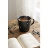 Cozy morning scene on a rustic wooden table, a matte charcoal gray mug with delicate white heart and dot pattern filled with steaming herbal tea, alongside an open book of poetry, natural light streaming thro