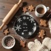 A rustic wooden kitchen table, dusted with flour, bathed in the soft, warm light of a winter afternoon, featuring a black ceramic plate with white snowflake designs and the inscription 'Letos na to pecu!', su