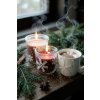 Close up lifestyle shot of a cozy winter scene on a rustic wooden table two lit, snowflake decorated candles in glass jars casting a warm, soft glow A steaming mug of hot cocoa sits beside them, topped with m