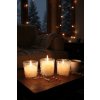 Cozy winter evening scene, soft glow of several snowflake decorated candles casting warm light on a rustic wooden coffee table, a steaming mug of hot chocolate with marshmallows nearby, a thick knitted blanke