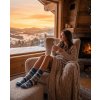 beautiful model girl chilling in cozy chalet wearing these wool socks. she is drinking tea and looking outside at beautiful hilly landscape view during sunset