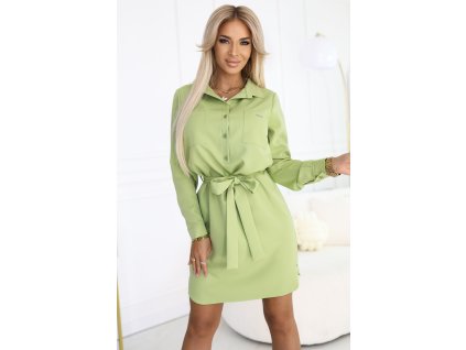 Modelka v zelených košeľových šatách so zaväzovaním v páse, golierom a dlhými rukávmi, s úsmevom v elegantnom prostredí.