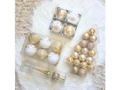 Arany és fehér karácsonyfadísz szett többféle gömbbel és arany csúcsdísszel fehér szőrmén elrendezve.