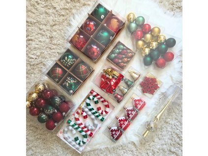 Piros, zöld és arany karácsonyfadíszek készlete – gömbök, házikók, cukorkapálcák, tobozok és egy arany csúcsdísz elhelyezve puha háttéren