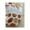 Kiscipós zsák elölről fotózva, fehér alapon barna péksütemény mintával és széles csipkedísszel.