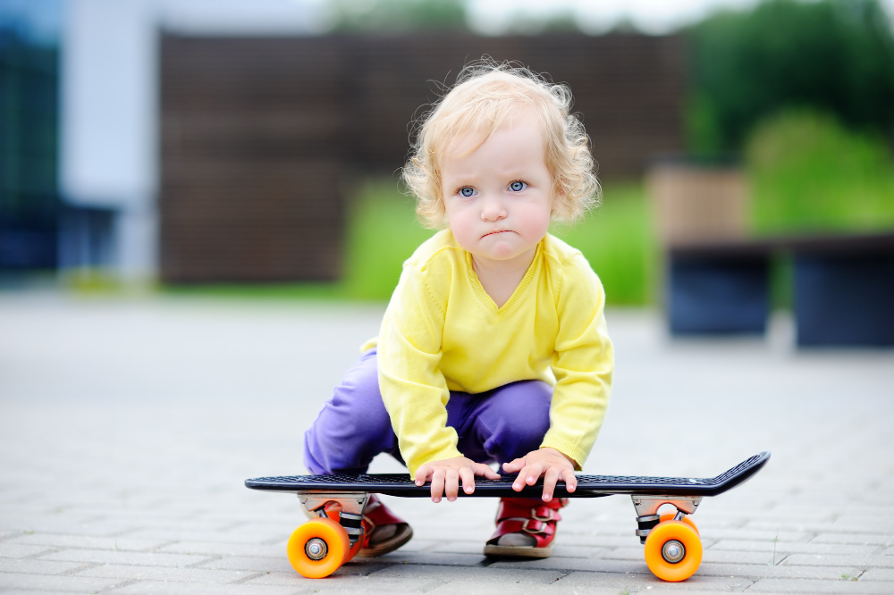 Malé dítě v barevném oblečení klečí u dětského skateboardu a zkoumá ho