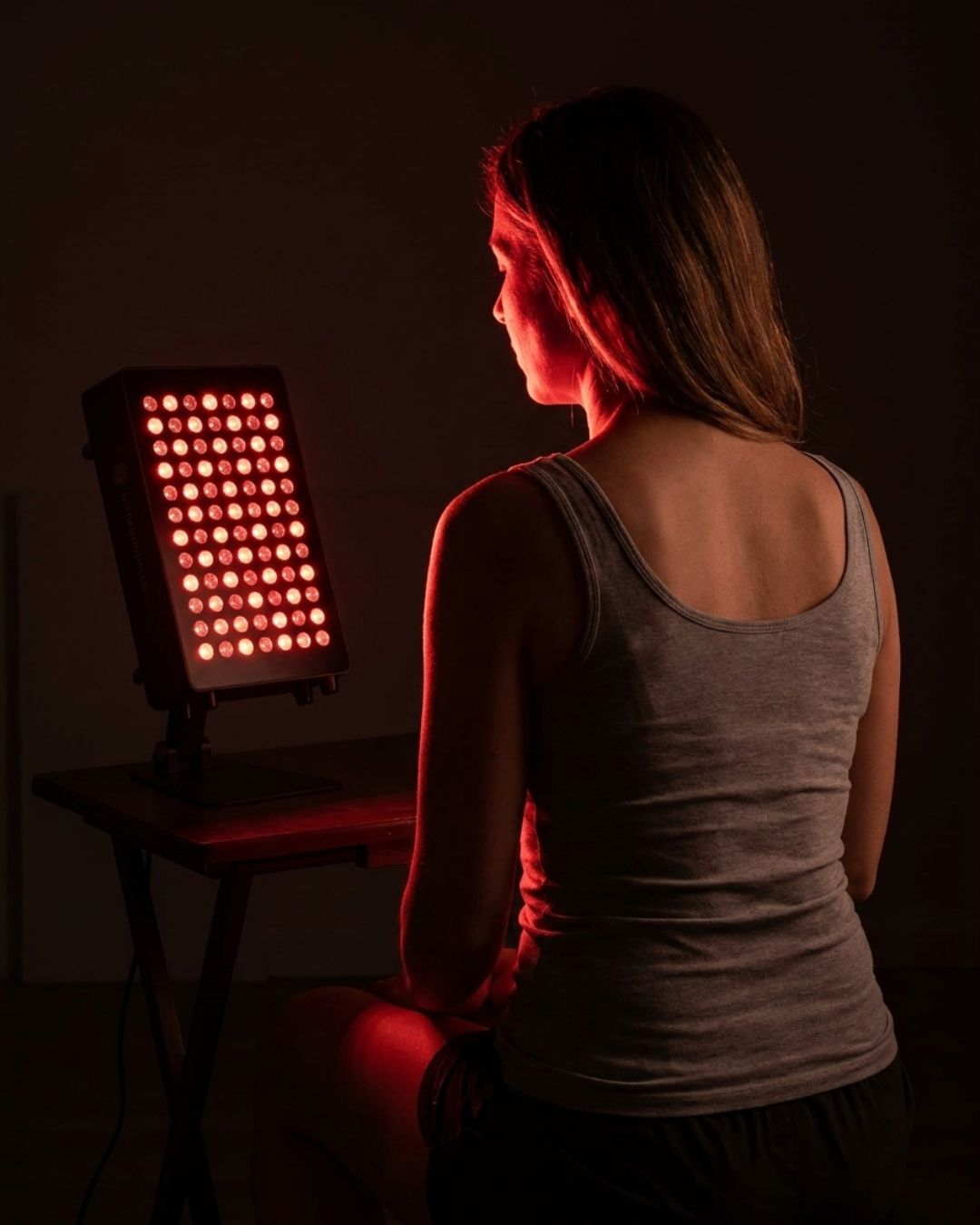 Woman using red light therapy on her face with a Mitochondriak Office infrared panel