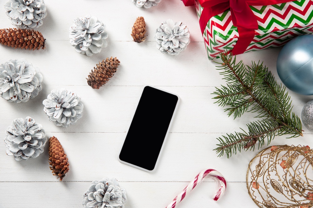 blank-empty-screen-smartphone-white-wooden-wall-with-colorful-holiday-s-decoration-gifts