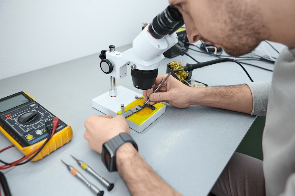 repairman-examining-mobile-phone-motherboard-microscope-laboratory
