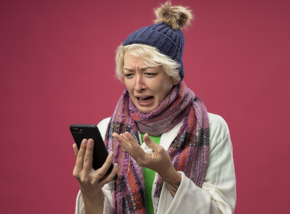 upset-sick-unhealthy-woman-with-short-hair-warm-scarf-hat-feeling-unwell-stressed-frustrated-lookign-her-smartphone-screen-standing-pink-background