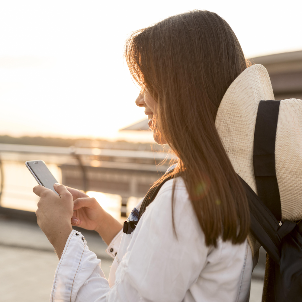 side-view-woman-with-hat-using-smartphone-while-traveling-alone