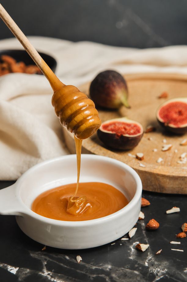 Med stékající z naběračky do misky, vedle čerstvé fíky