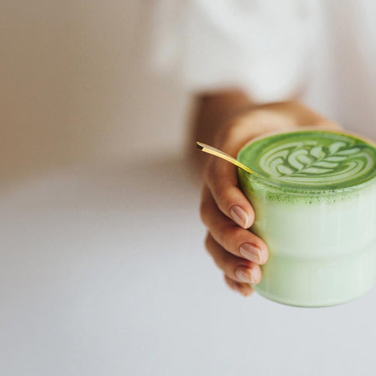 Dłonie trzymają szklany kubek z matcha latte