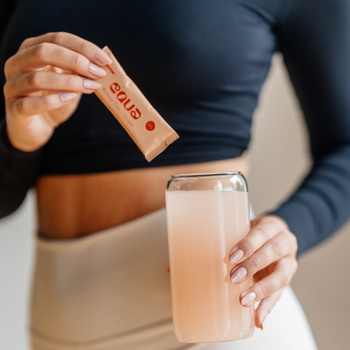Kobieta trzyma saszetkę Recharge Tonic + Creatine i szklankę