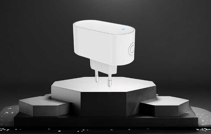 Bílá brána MOES MPH-S1 s oválným zaobleným tělem, bočním kulatým tlačítkem a dvěma kovovými kolíky pro zapojení do elektrické zásuvky, umístěná na černém podstavci