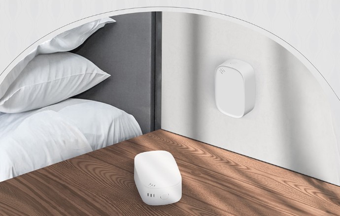 Senzor teploty a vlhkosti MOES ZSS-S01-TH-C ZigBee umístěný na nočním stolku vedle postele, zatímco druhý senzor je připevněný na stěně