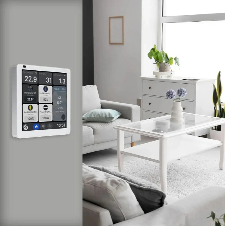 Shelly Wall Display X1i stříbrný instalovaný na stěně v obývacím pokoji. Na dotykovém displeji jsou zobrazeny údaje o teplotě, vlhkosti, spotřebě energie, počasí a připojených chytrých zařízeních.